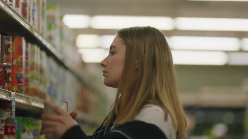 Young woman dances slightly as she listens to music while putting cans on grocery store shelf