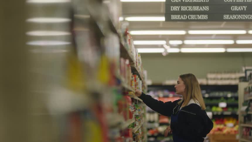 Young girl working at a small supermarket restocking the shelves