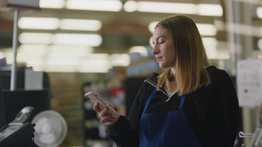 Women stand in a store waiting while one looks at her cellphone