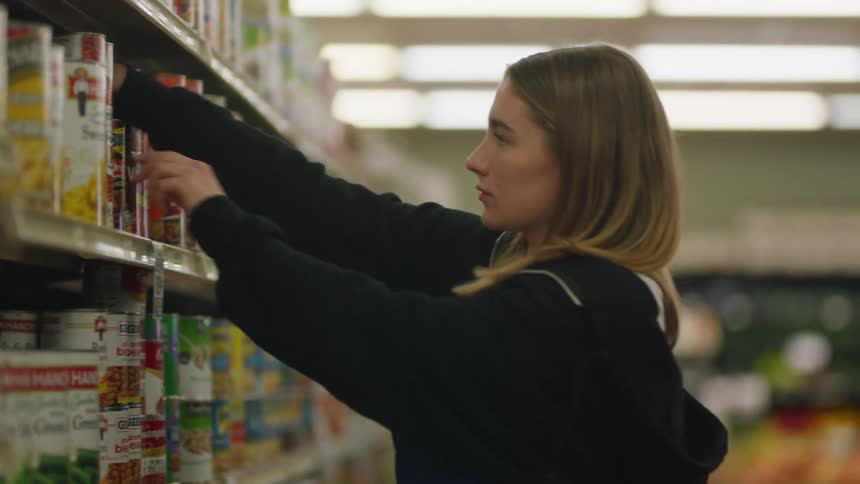 A woman is rearranging cans on the shelves of a grocery store