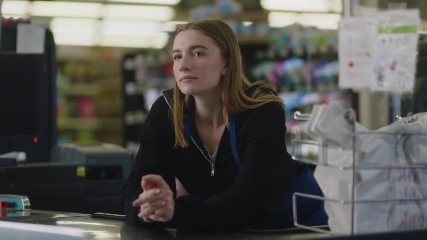 A young female grocery store employee waits patiently at the checkout stand