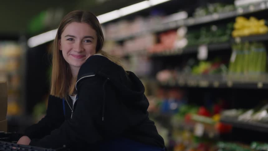 A store worker is leaning on a cart near some vegetables