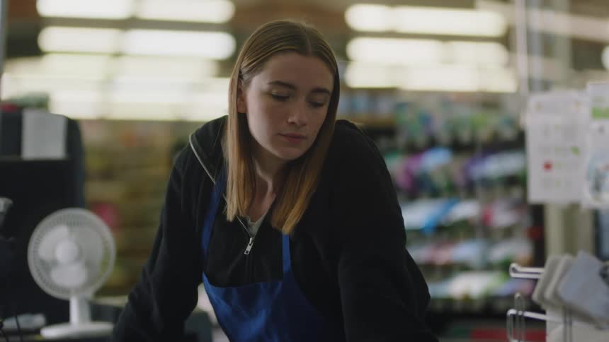 A young woman is standing against a counter in a store looking bored