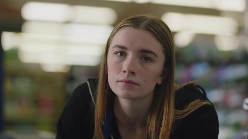 Close up of a young blonde woman looking at the camera inside a small store