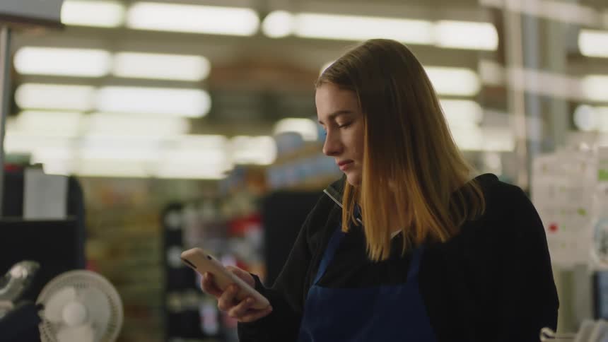 The girl is using her cell phone at the register