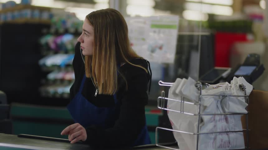 A cashier puts her phone away and stands smiling to greet a customer