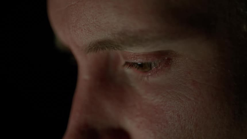A man rubs his eyes with his hands as he sits in the dark