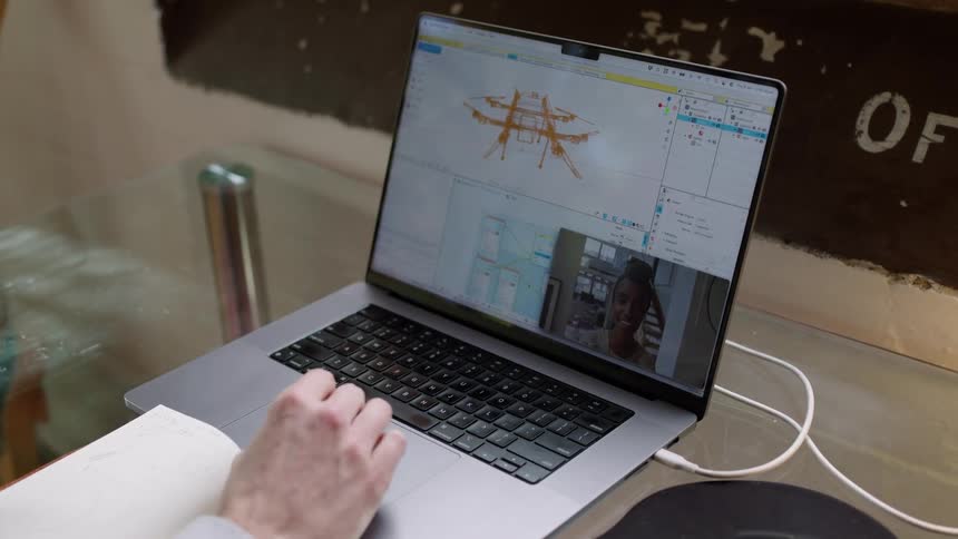 A man has a note book open in front of his laptop as he talks to a woman on the screen