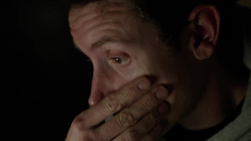 A man rubs his eyes looking tired in the glow from a computer