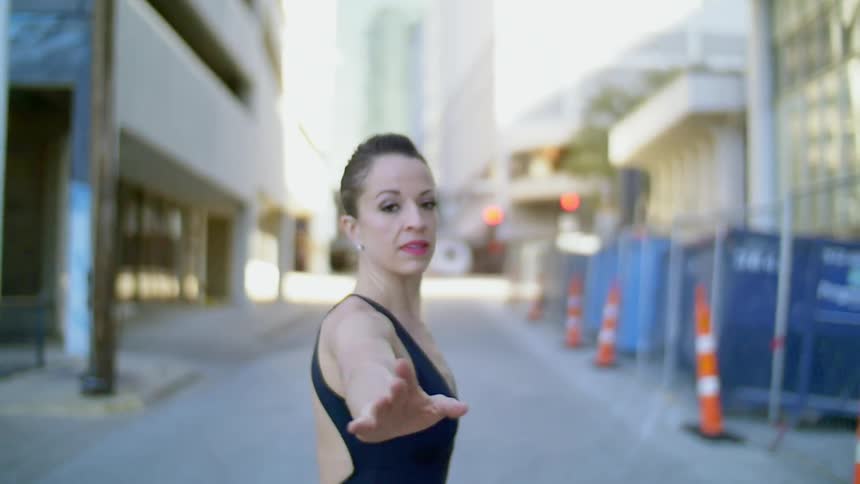 A woman is ballet dancing down a city street