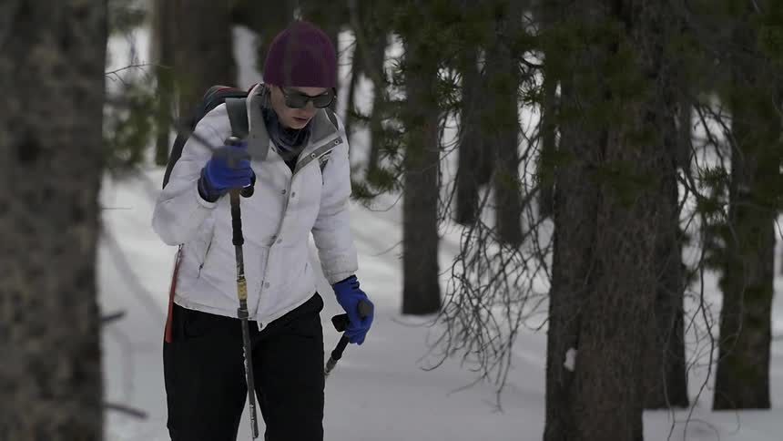 A woman is hiking downhill in the snow