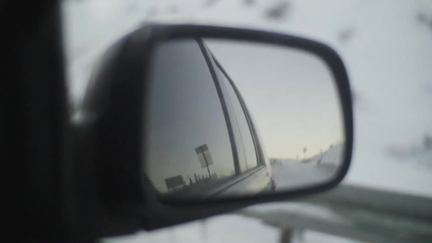 A snow covered road can be seen in the rear view mirror