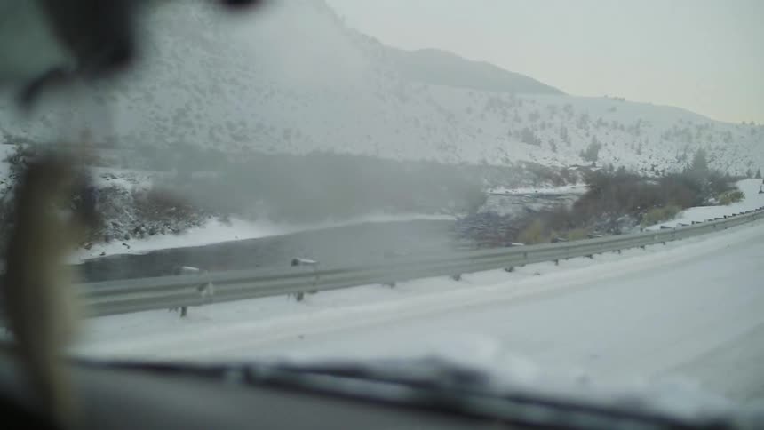 A car is traveling down a snow covered road on a cloudy day