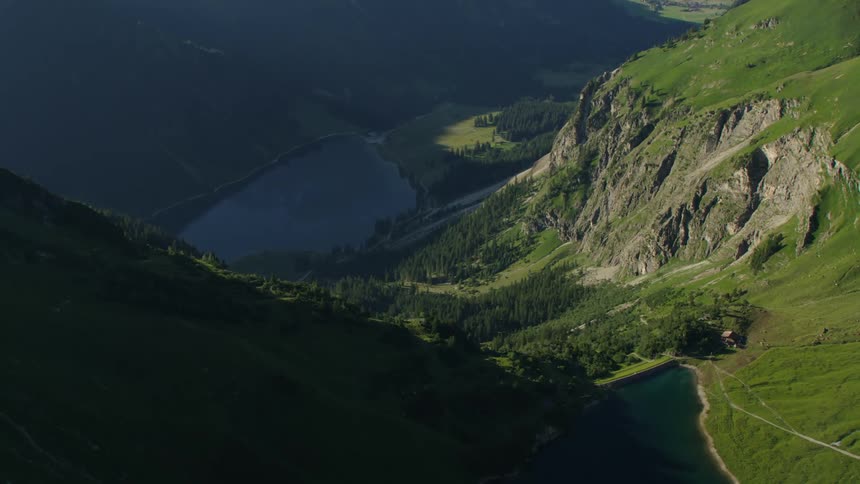 Forest sits at base of cliff between lakes in green valley