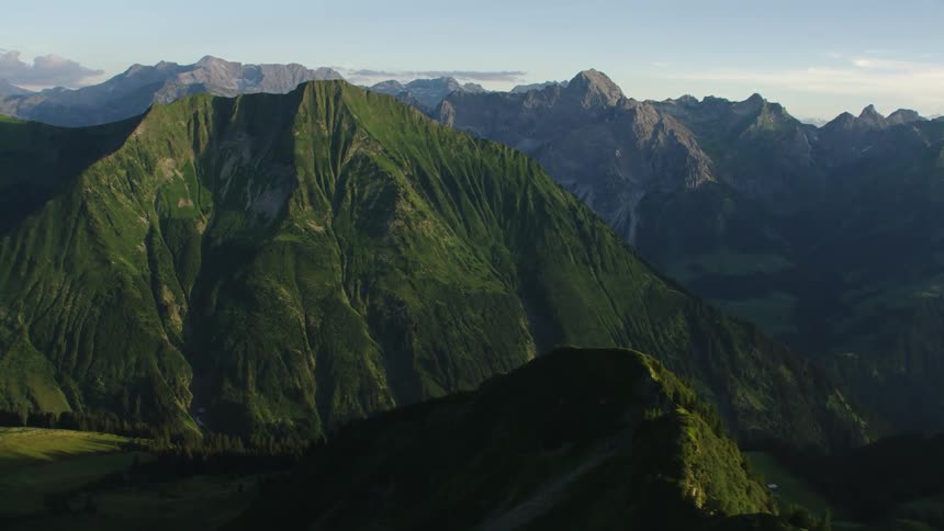Grass covers a mountain ridge and there are mountains in the distance with peaks high in the sky