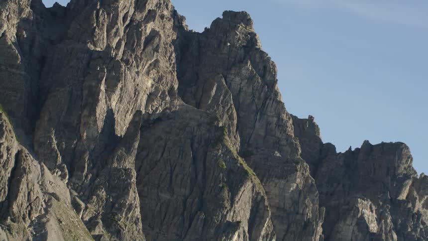 Jagged rock atop a mountain slope under a clear daytime sky