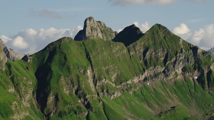 A towering rocky mountain range is covered in dense vegetation