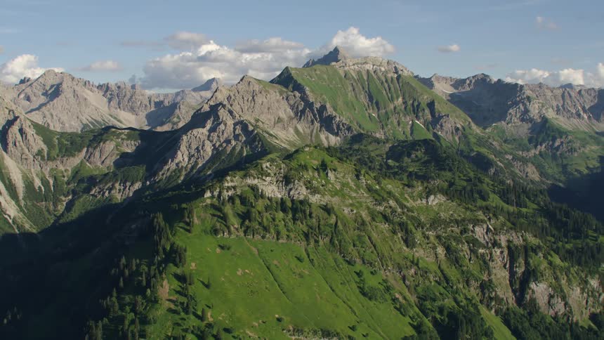 Grass grows on a mountain ridge and there are mountains in the distance with peaks high in the sky