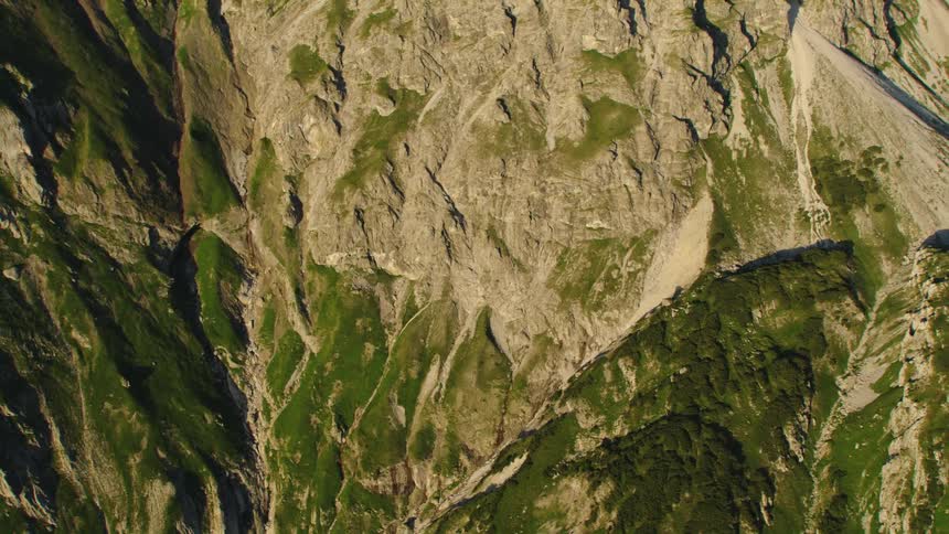 A jagged mountain slope covered in patches of vegetation during the day