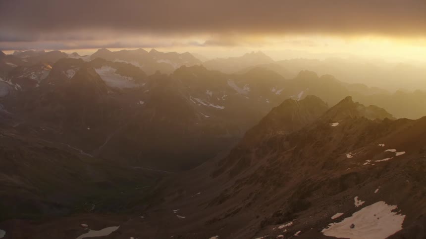 Jagged mountain ridges dusted with snow under a hazy cloudy sky
