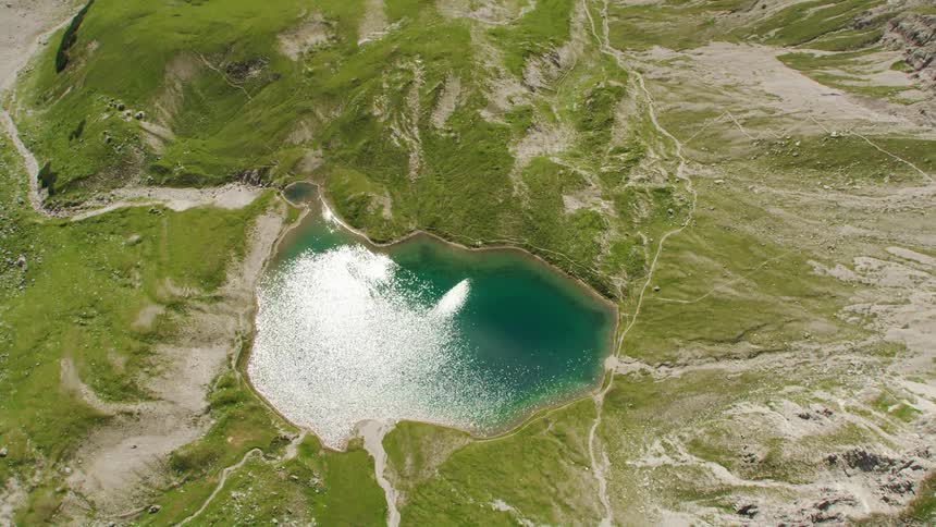 Aerial view of sunlight reflecting on the clear surface of a small lake in the mountains