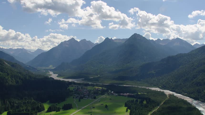 Aerial view of sunlight coming through the clouds over a field close to a river in the mountains