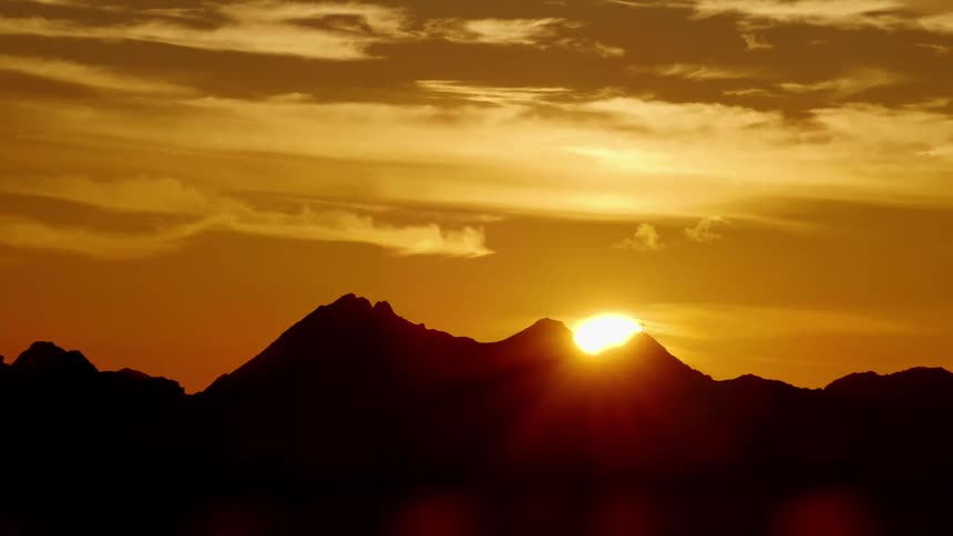 Aerial view of the sun setting over the silhouette of a mountain range at sunset