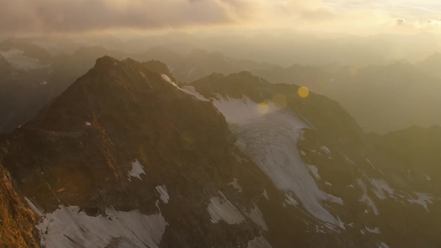 Aerial view of clouds floating over snowy mountains at sunset