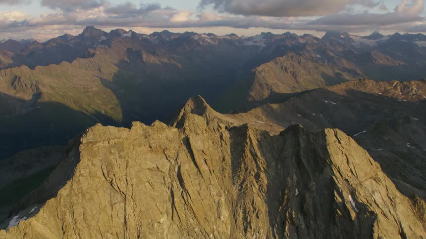 The sun shines on a mountain ridge and there are mountains in the distance
