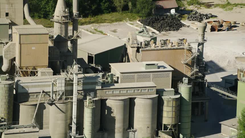 Two large piles of tires sit on concrete near large factory