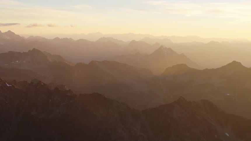 Dense fog covers craggy mountain range stretching to the horizon under a yellow sky