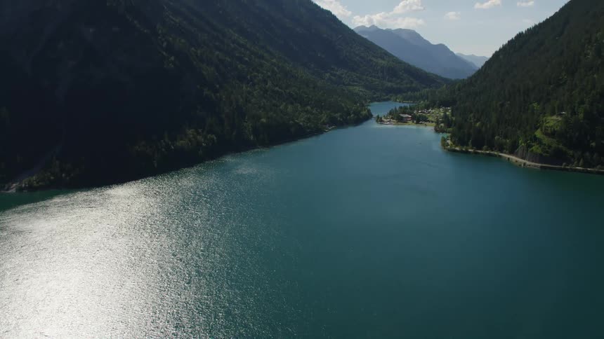 The sun shines brightly on a river running between mountains and there are mountains on the horizon