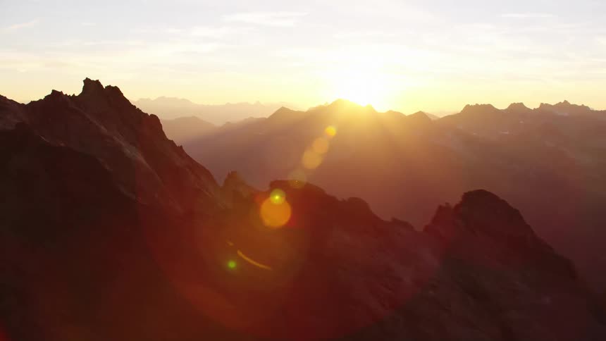 Sun shines over craggy mountains in range turning sky and fog yellow