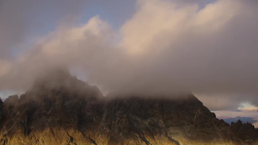 Clouds cover the shaded jagged mountain ridge