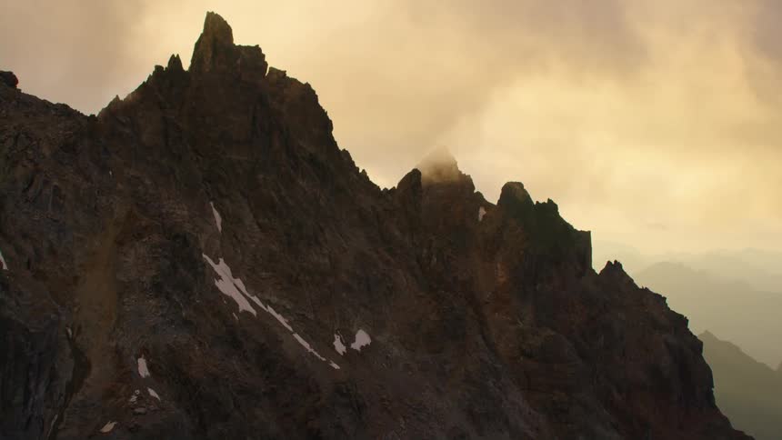 Aerial view of the jagged peak of a tall mountain top covered in clouds at morning