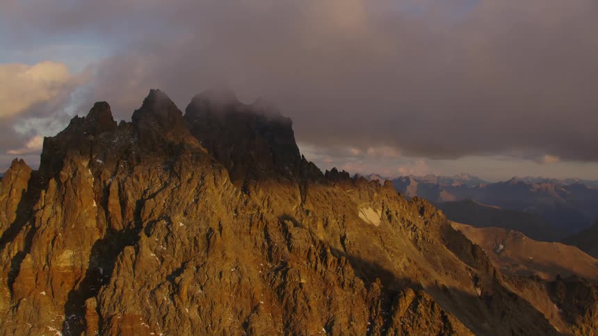 A mountain ridge stands tall with peaks high in the clouds and there are mountains on the horizon