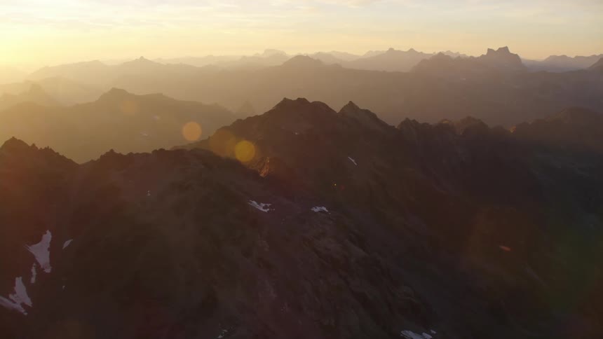 Mountain ranges with peaks high in a hazy sky illuminated by orange sunlight