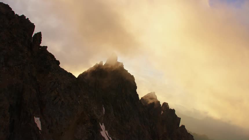 Aerial view of clouds floating over steep mountains at sunset