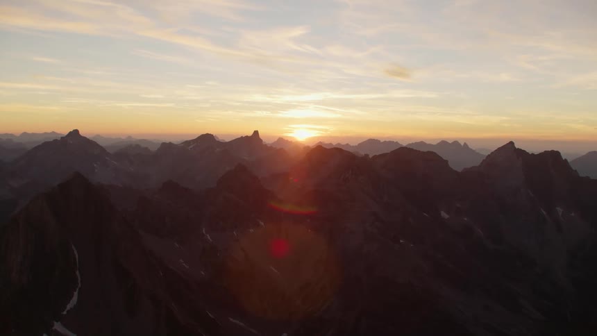 The sun setting and glowing on the horizon above jagged mountain peaks