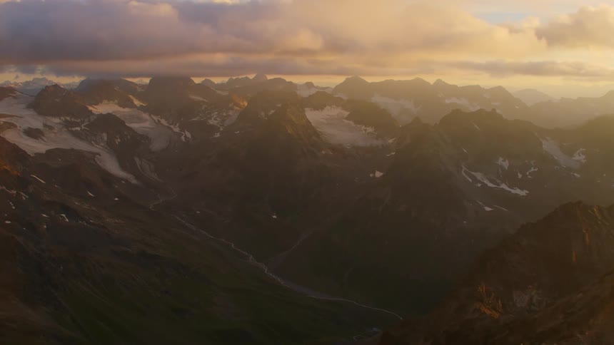 Aerial view of the rugged slopes of a mountain range under the clouds at evening