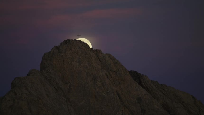 Aerial view of the full moon rising over a cross atop a mountain at night