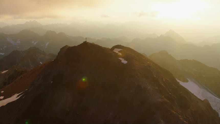 Aerial view of a cross atop the summit of a mountain range at sunset