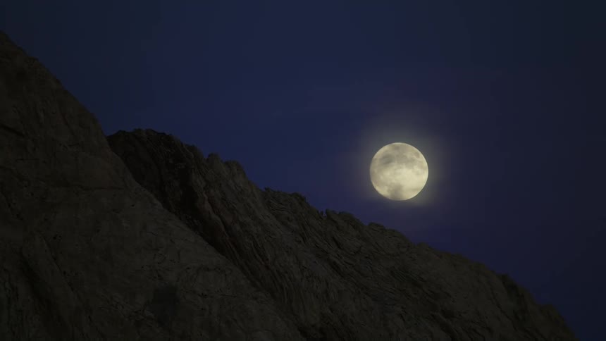 The full moon is shining brightly in the sky above mountains