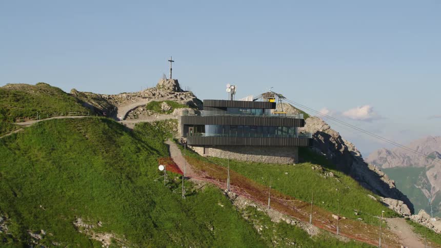 A building is on top of a mountain and there is a cross near it and mountains on the horizon