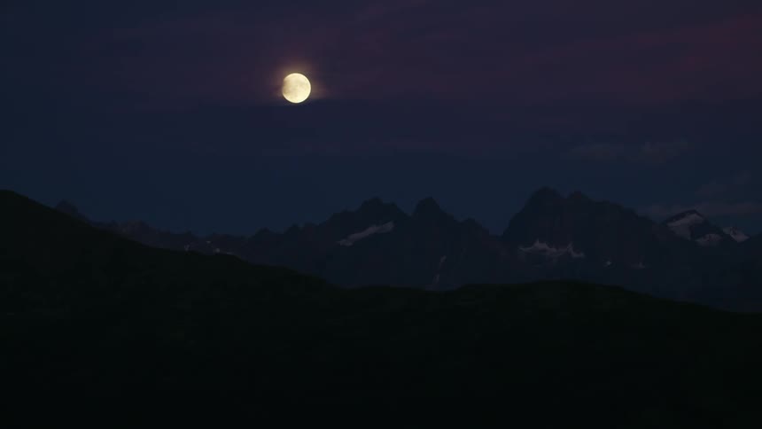 The full moon is shining brightly in the sky above mountains