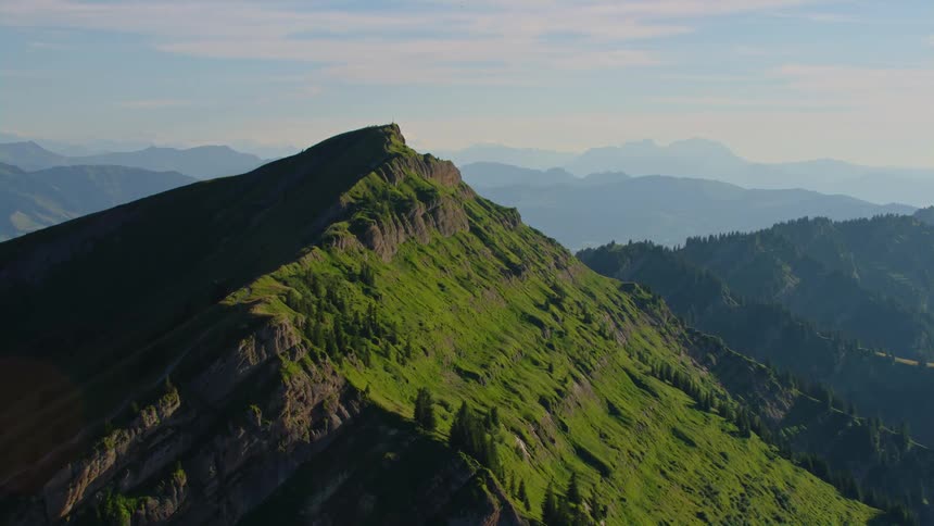 A jagged mountain peak atop a slope covered in low vegetation during the day