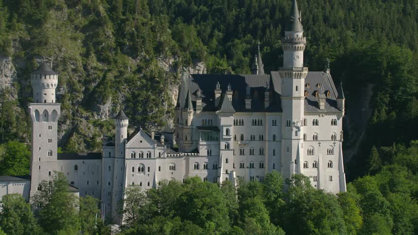 Castle sits among conifer forest on mountain top in a mountain range