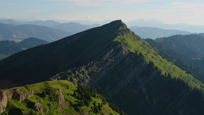 A mountain peak that is covered in grass and trees stands tall on a sunny day