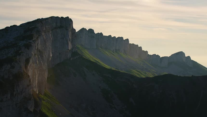 Rocky peaks on a mountain range reach high in a cloudy sky and there are mountains on the horizon
