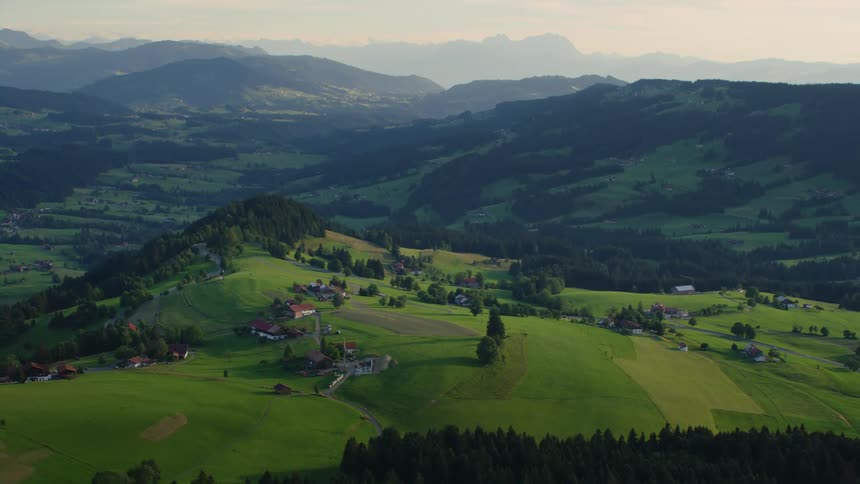 Aerial view of houses on the fields in the hills near a mountain range at evening